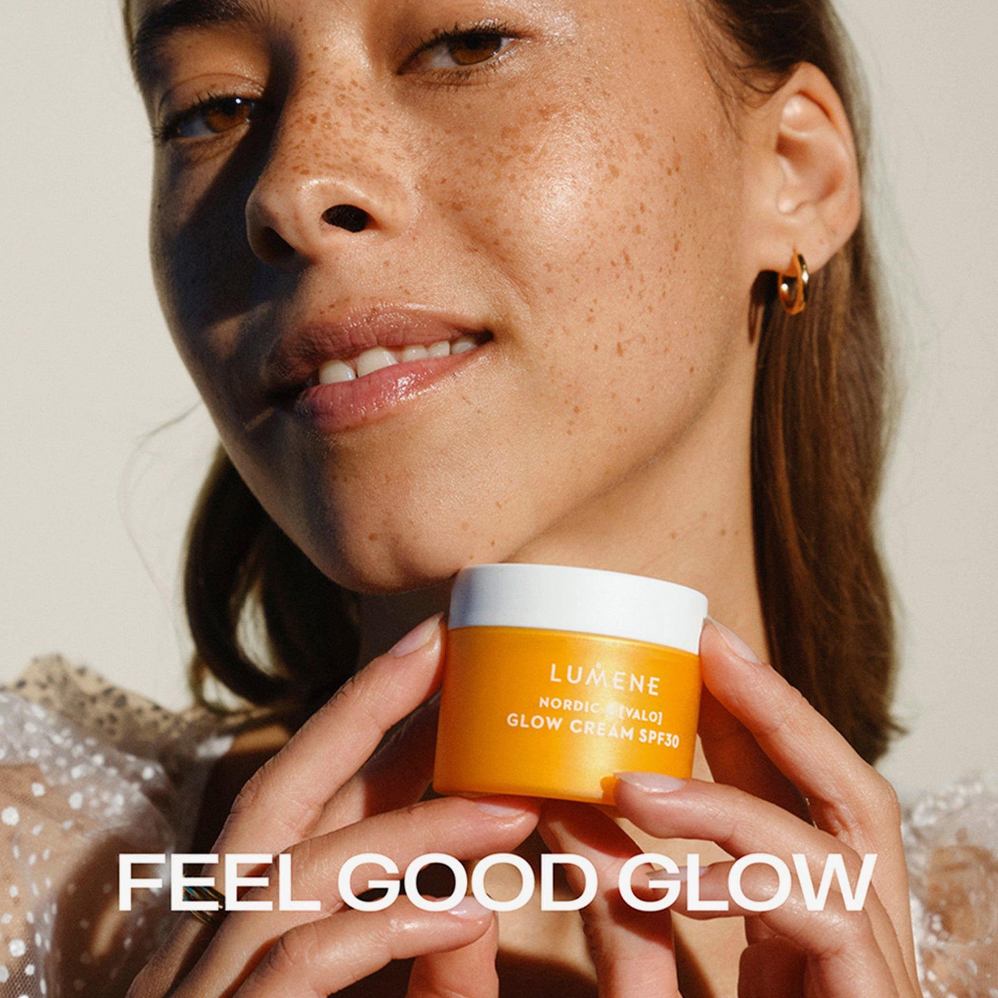 Donna che tiene un vasetto di crema giallo. Scritta: LUMENE, NORDIC-C [VALO] GLOW CREAM SPF30. Testo: FEEL GOOD GLOW.