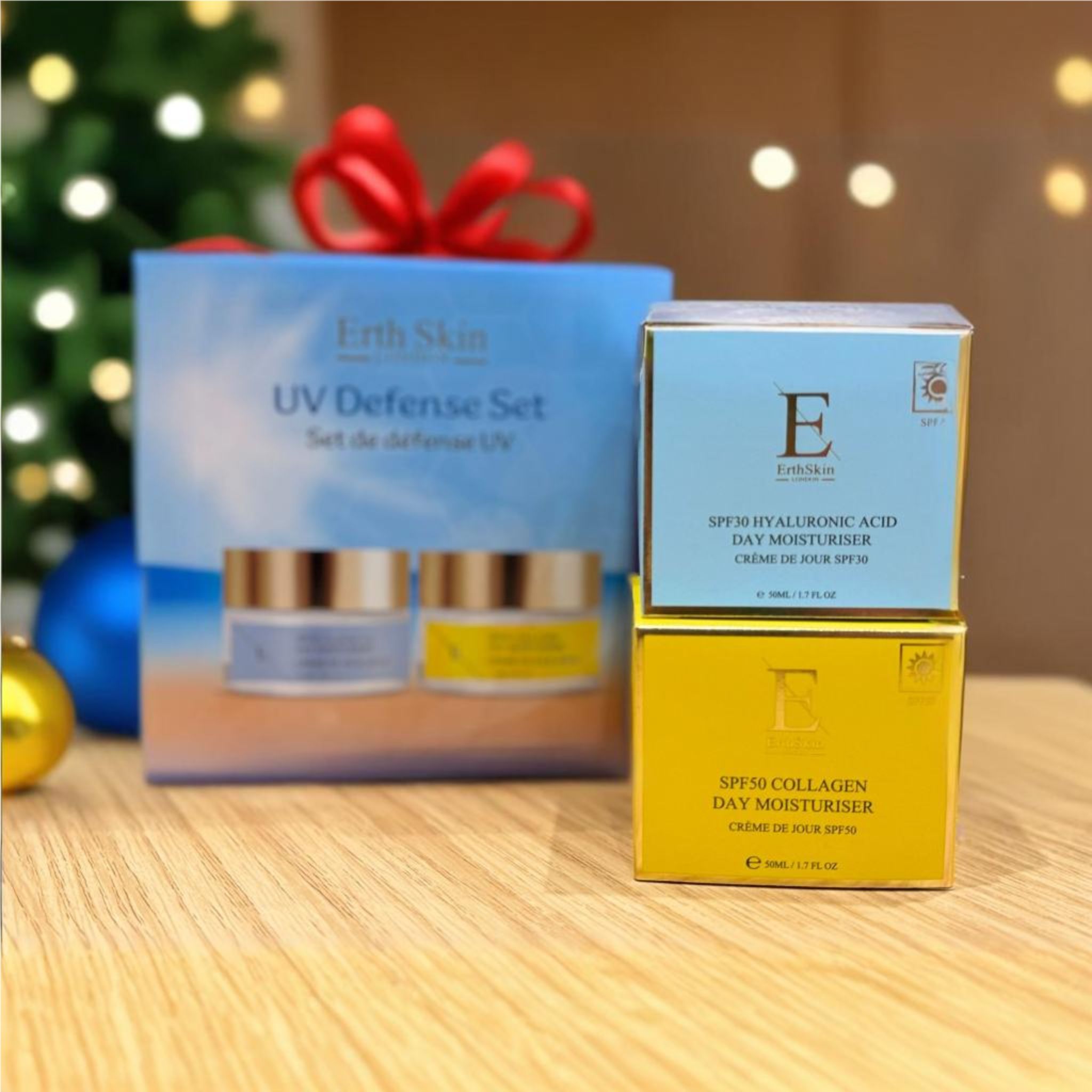 Set regalo con due creme e due scatole. "Erth Skin UV Defense Set". Creme con coperchi dorati ed etichette. Decorazioni natalizie sullo sfondo.