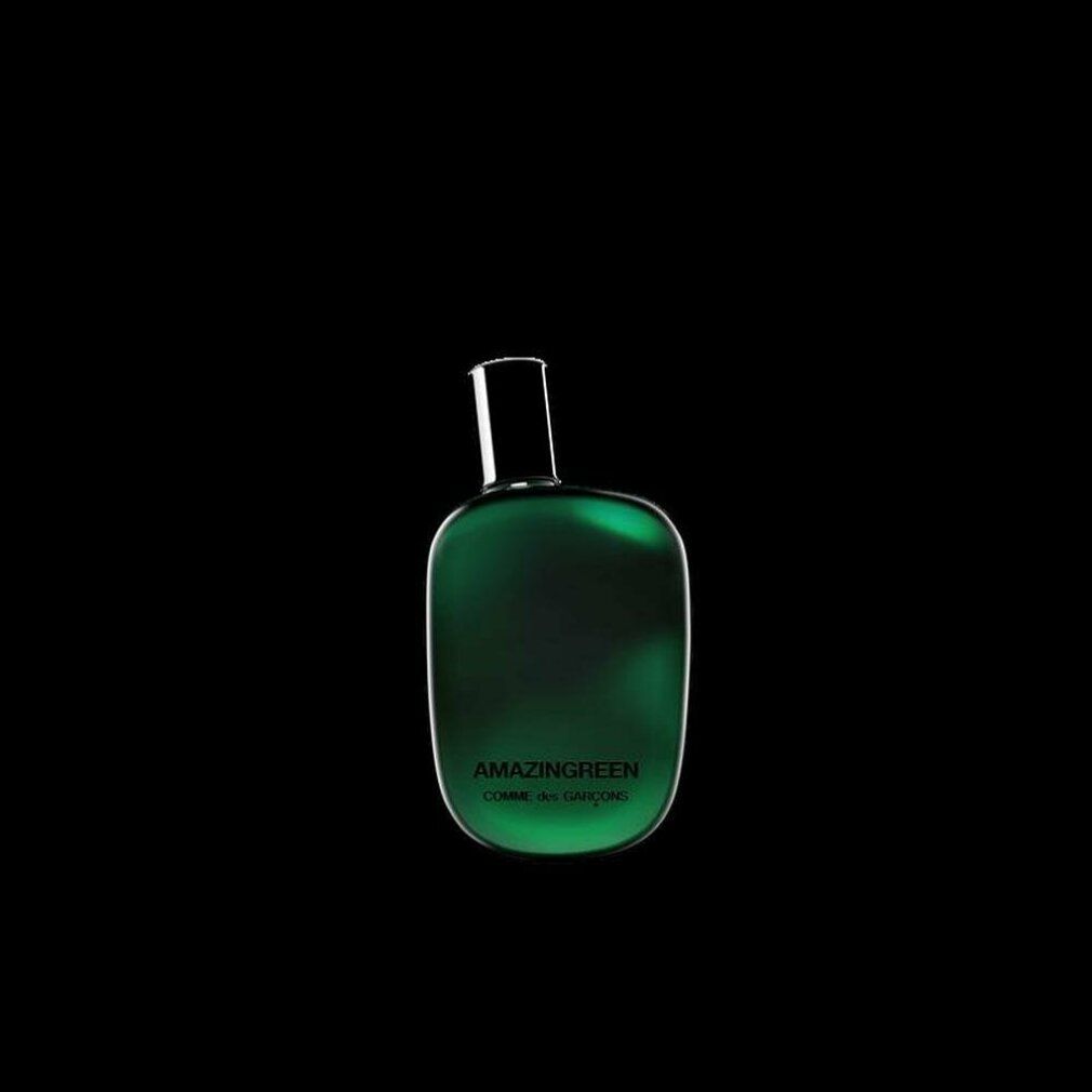 Flacone di profumo verde con tappo nero su sfondo nero. Scritta: AMAZINGREEN, COMME des GARÇONS.