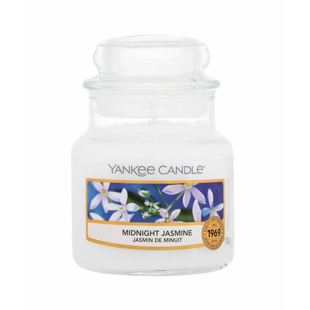 Piccola candela profumata in vaso con coperchio. Etichetta con motivo floreale e scritta "Midnight Jasmine". Marchio: Yankee Candle. Adesivo dorato.