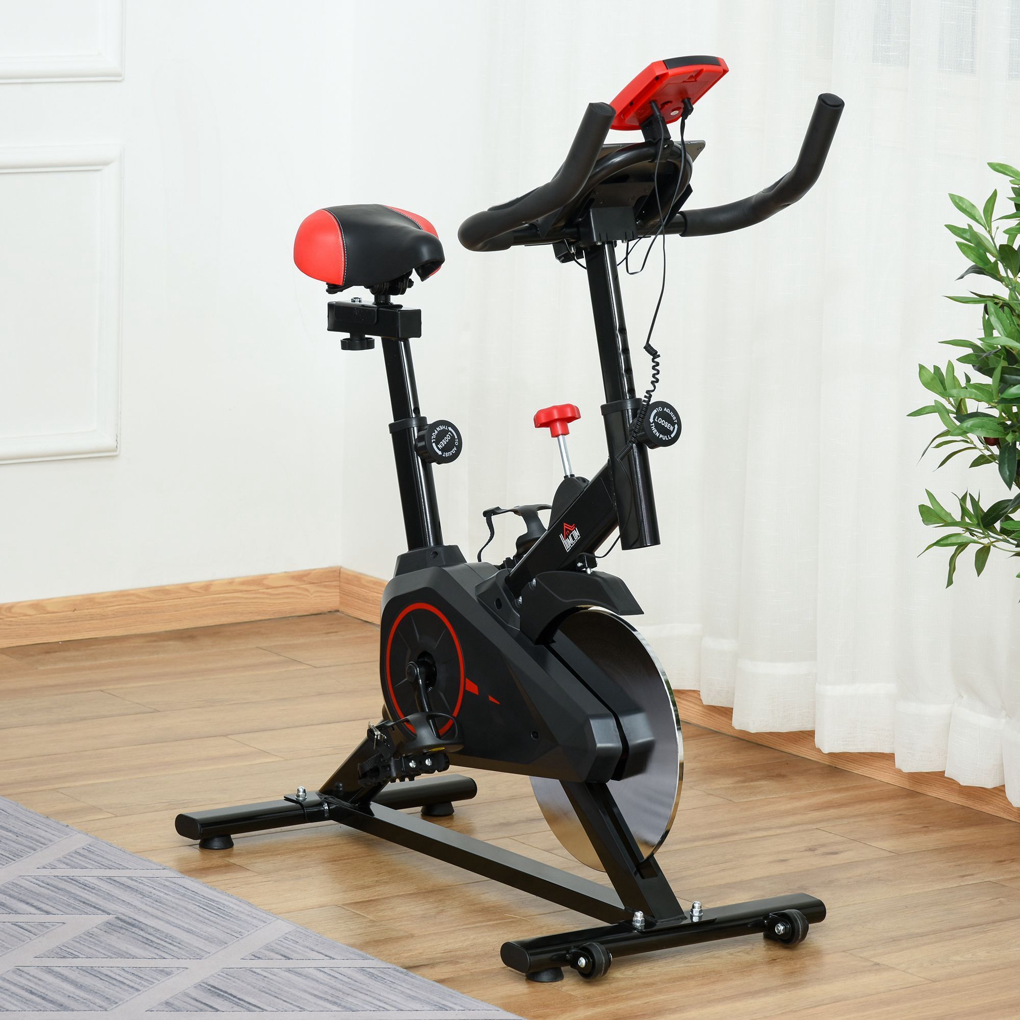 Bicicletta fitness nera con sella e manubrio rossi. Schermo LCD e sensore di frequenza cardiaca. Su pavimento in legno.