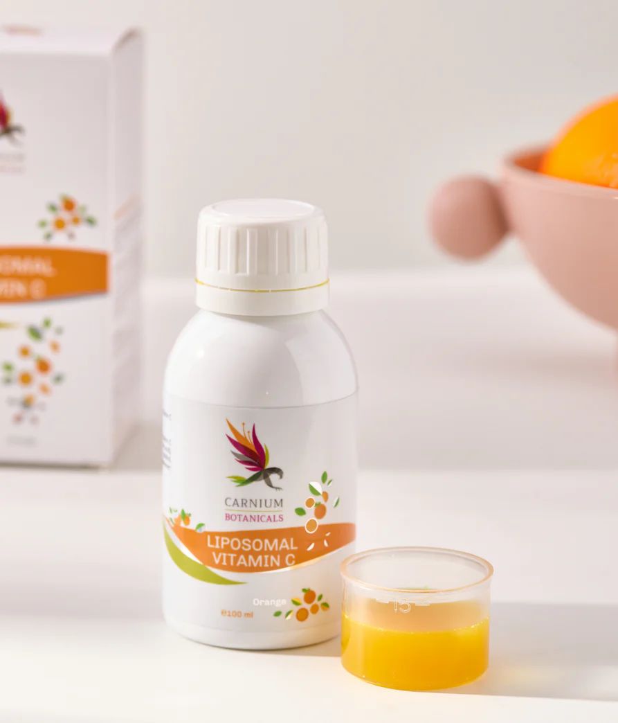 Flacone bianco con etichetta gialla. Carnium Botanicals Liposomal Vitamin C. Misurino con liquido accanto.