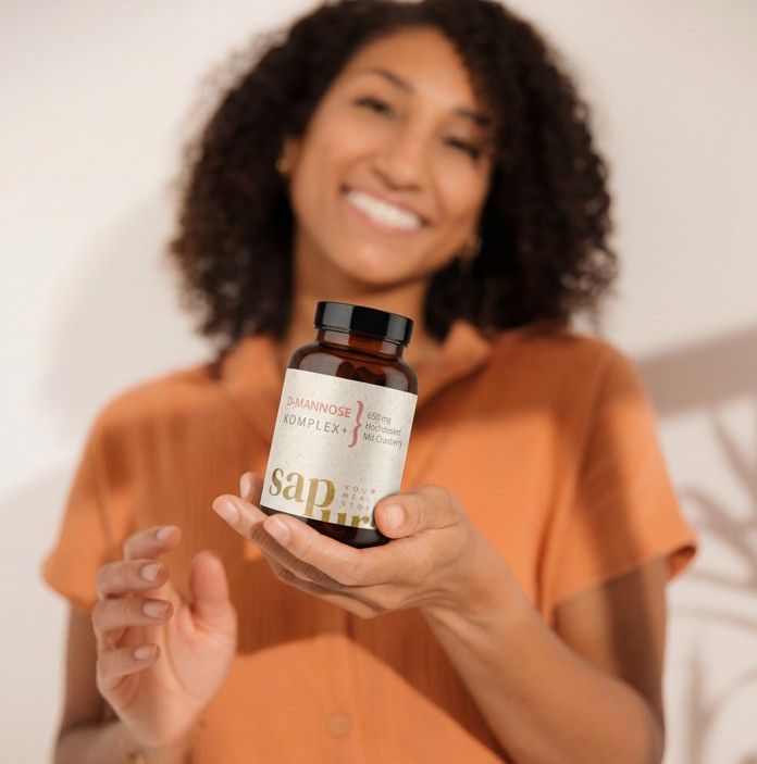 Una donna sorridente tiene una bottiglia di D-Mannose Komplex+ 650mg con Cranberry.