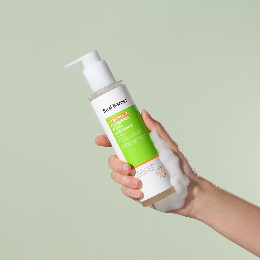 Flacone bianco-verde con dosatore, tenuto in mano. Schiuma sulla mano. Testo: Real Barrier, Control-T Cleansing Foam.