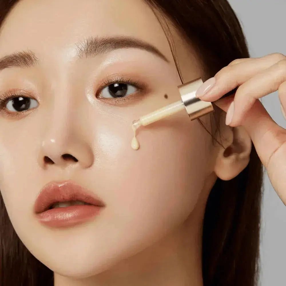 Primo piano di una donna che applica il siero sul viso con una pipetta. La pelle è lucida. Pipetta dorata.