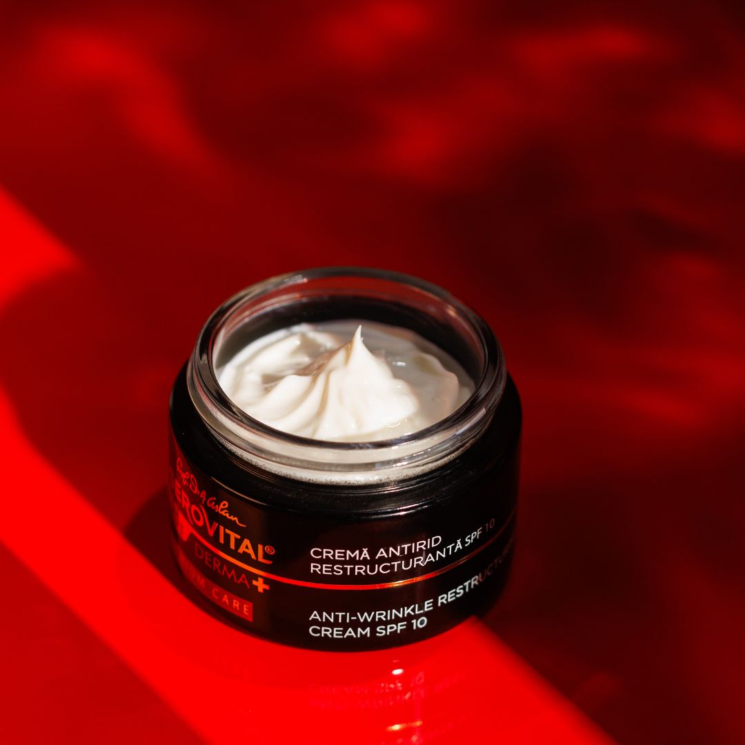 Vasetto di crema nero aperto con crema bianca su sfondo rosso. Testo: Gerovital H3 Derma+, Crema ristrutturante anti-rughe SPF10.