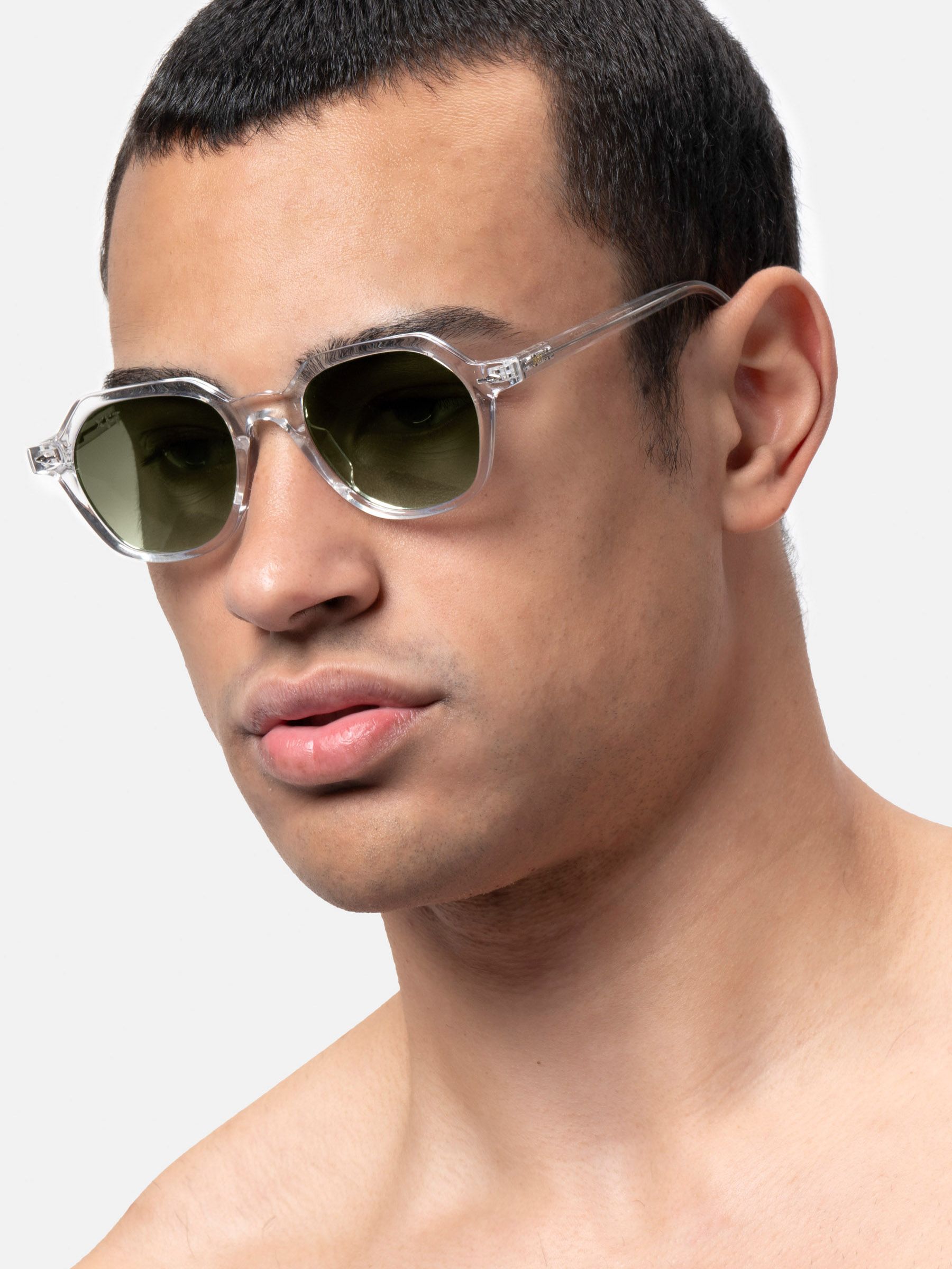 Primo piano di uomo con occhiali da sole con lenti esagonali e montatura trasparente. Lenti verdi.