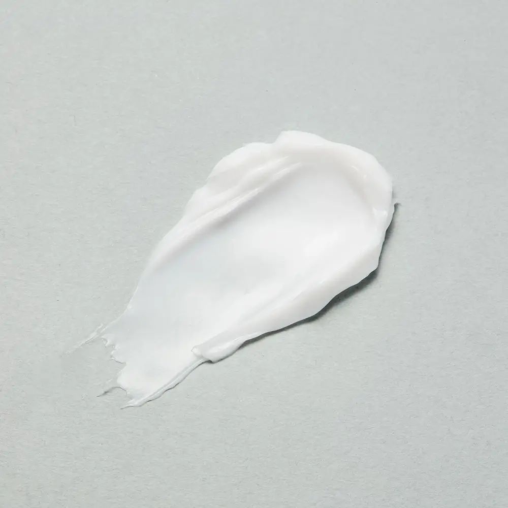 Macchia di crema bianca su sfondo grigio. Consistenza visibile.