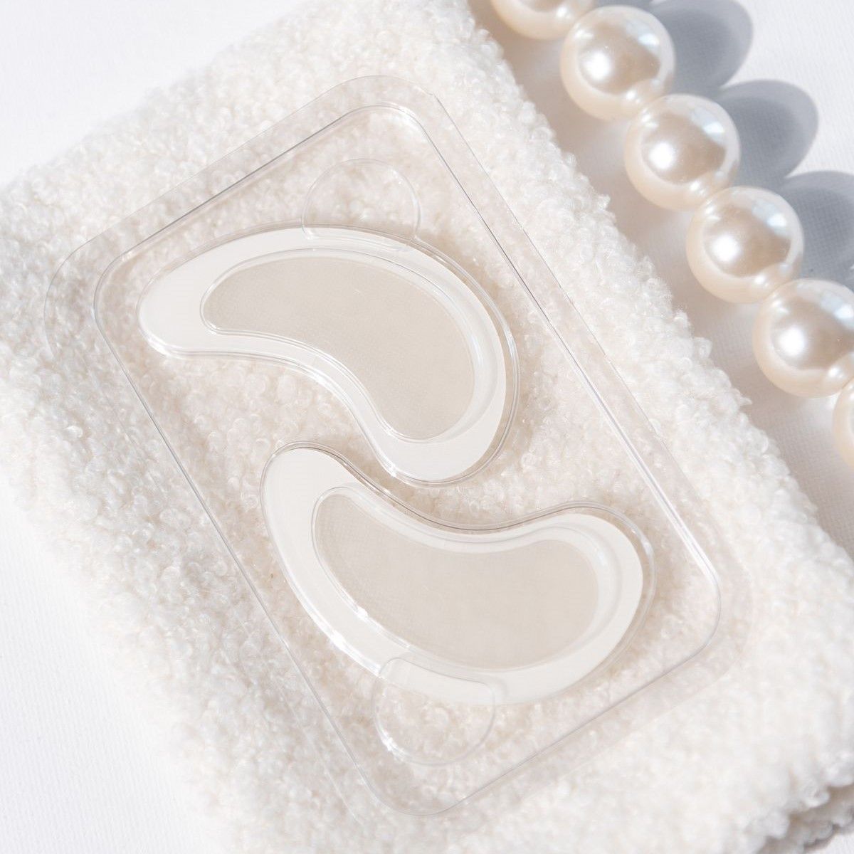 Due patch occhi in confezione trasparente. Su un asciugamano bianco con perle.