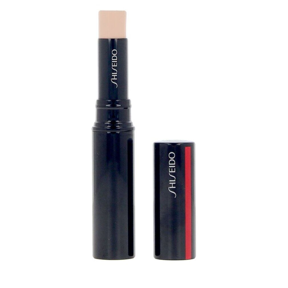 Correttore in stick. Stick blu scuro con prodotto beige. Tappo accanto. Logo Shiseido su stick e tappo. Striscia rossa sul tappo.