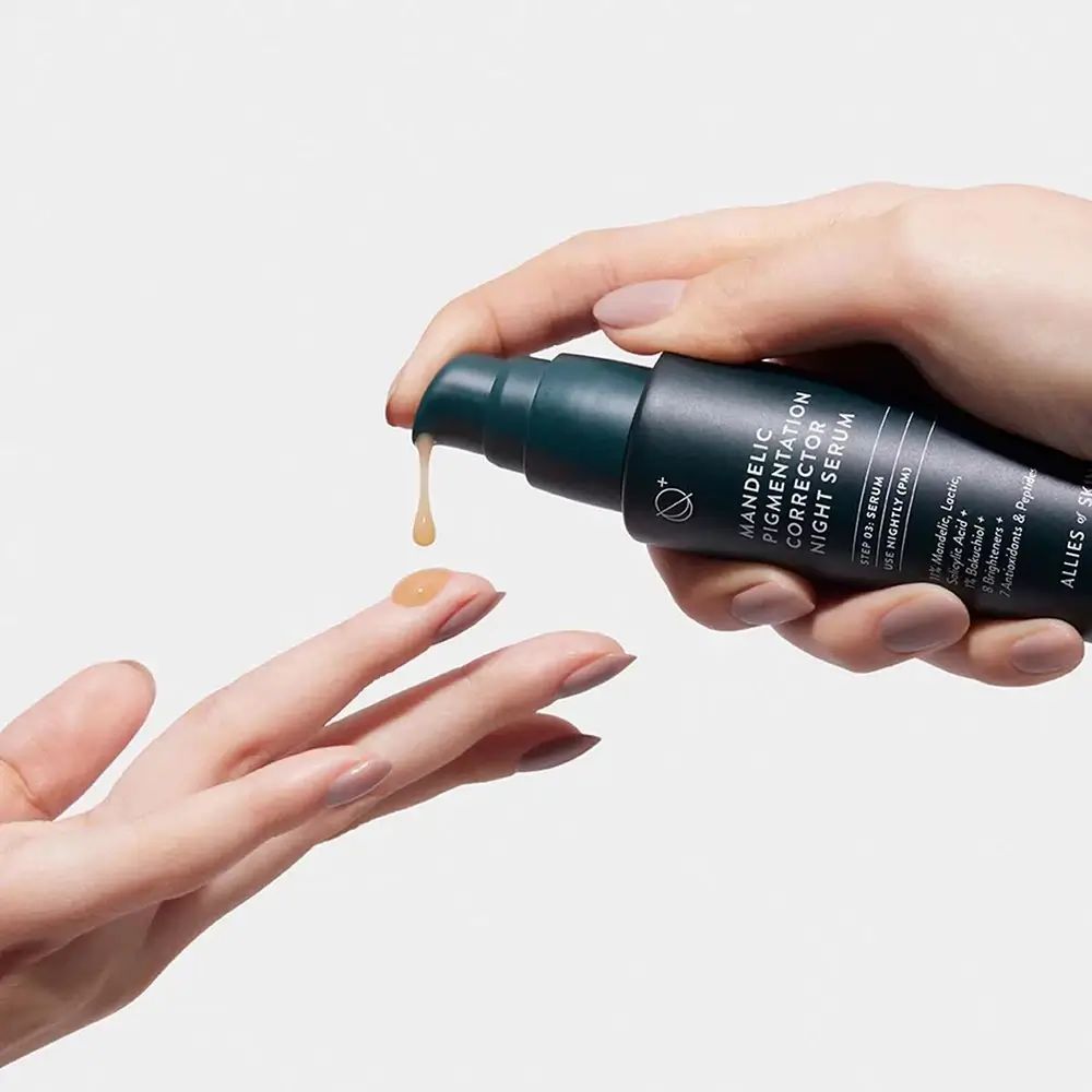 Mani che tengono una bottiglia di siero. Goccia di siero. Testo: Mandelic Pigmentation Corrector Night Serum. Bottiglia verde.