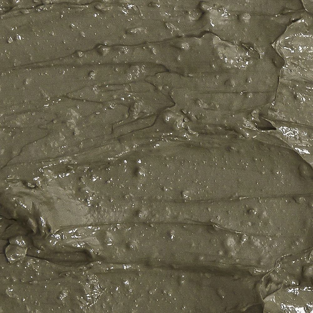 Texture di una maschera all'argilla grigio-verde con striature e ondulazioni visibili.