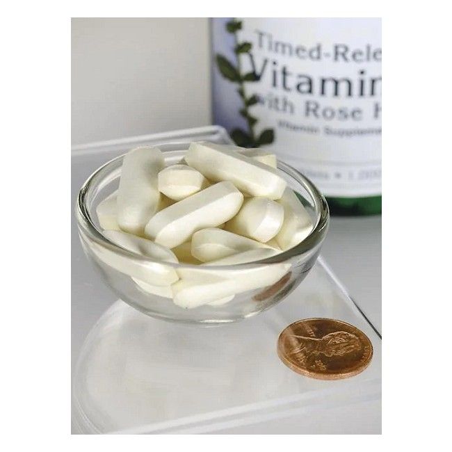 Ciotola di vetro trasparente con compresse bianche. Accanto, una moneta. Sullo sfondo, flacone con etichetta del prodotto.