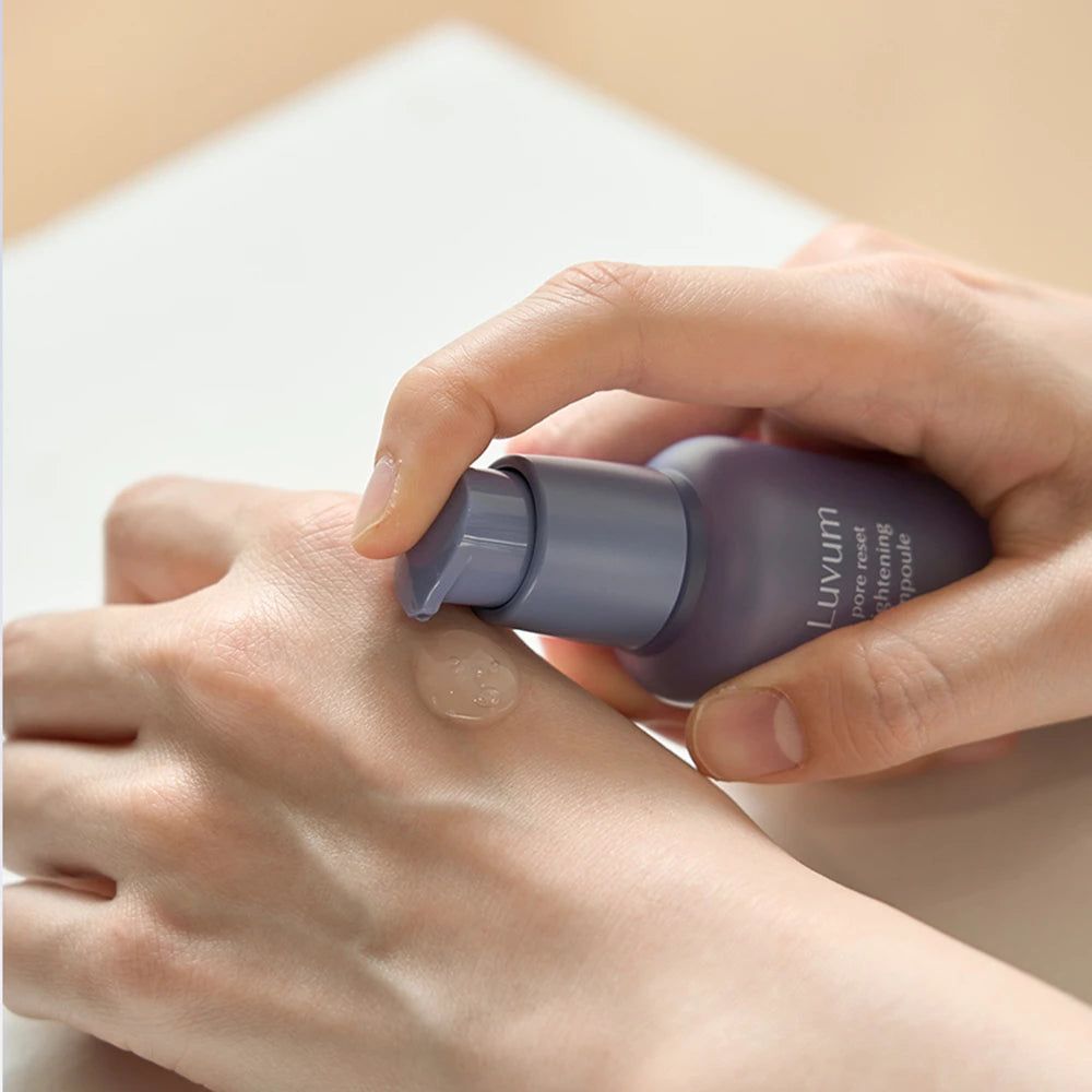 Mani che tengono una bottiglia viola. Un siero viene applicato sul palmo. La bottiglia reca la scritta "Luvum pore reset tightening ampoule".