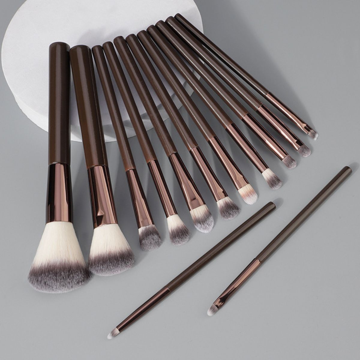 Un set di undici pennelli per il trucco marroni con finiture metalliche e setole morbide.