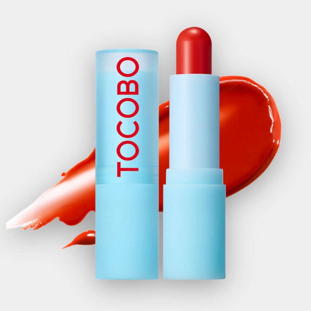 Due stick di balsamo per labbra, uno aperto, uno chiuso. Rossetto rosso. Custodie blu. Macchia di colore rosso accanto.