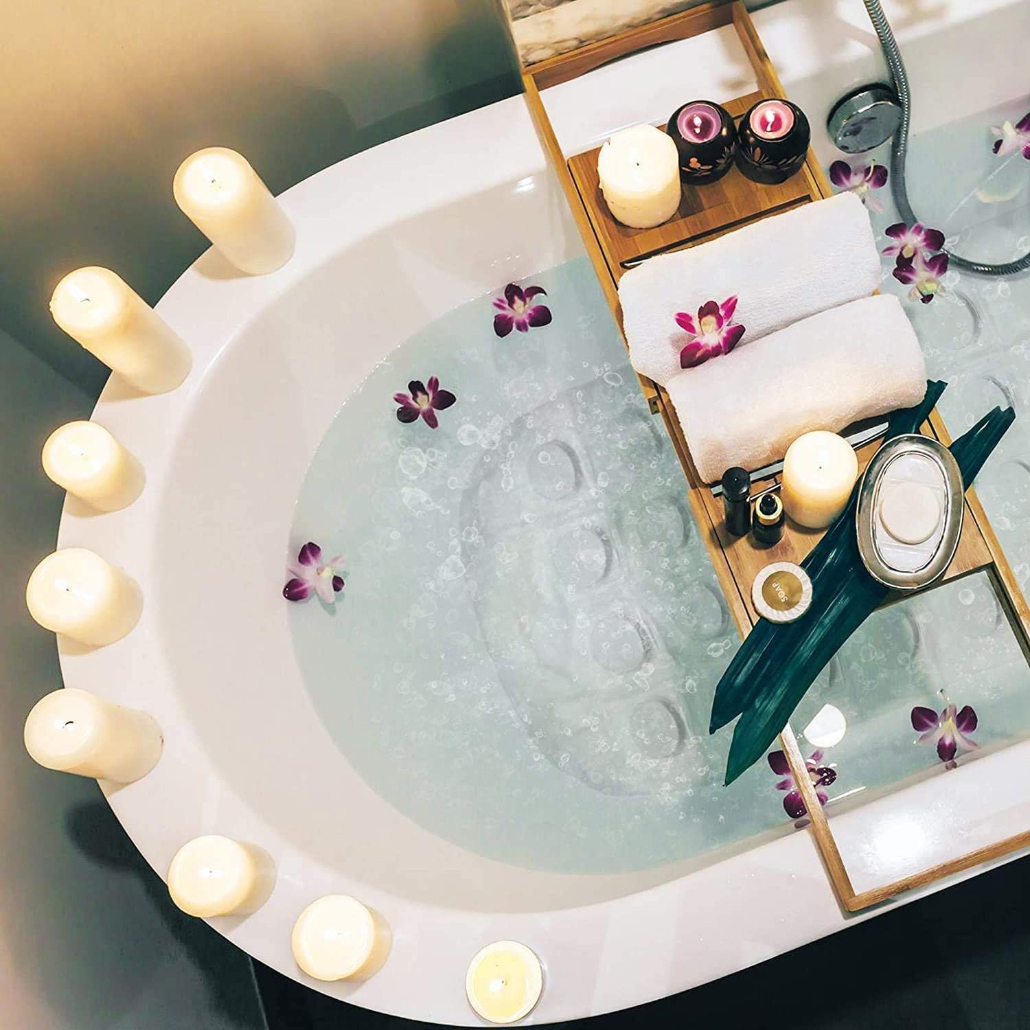 Vasca da bagno con acqua, candele, asciugamani, fiori e accessori da bagno su un vassoio.