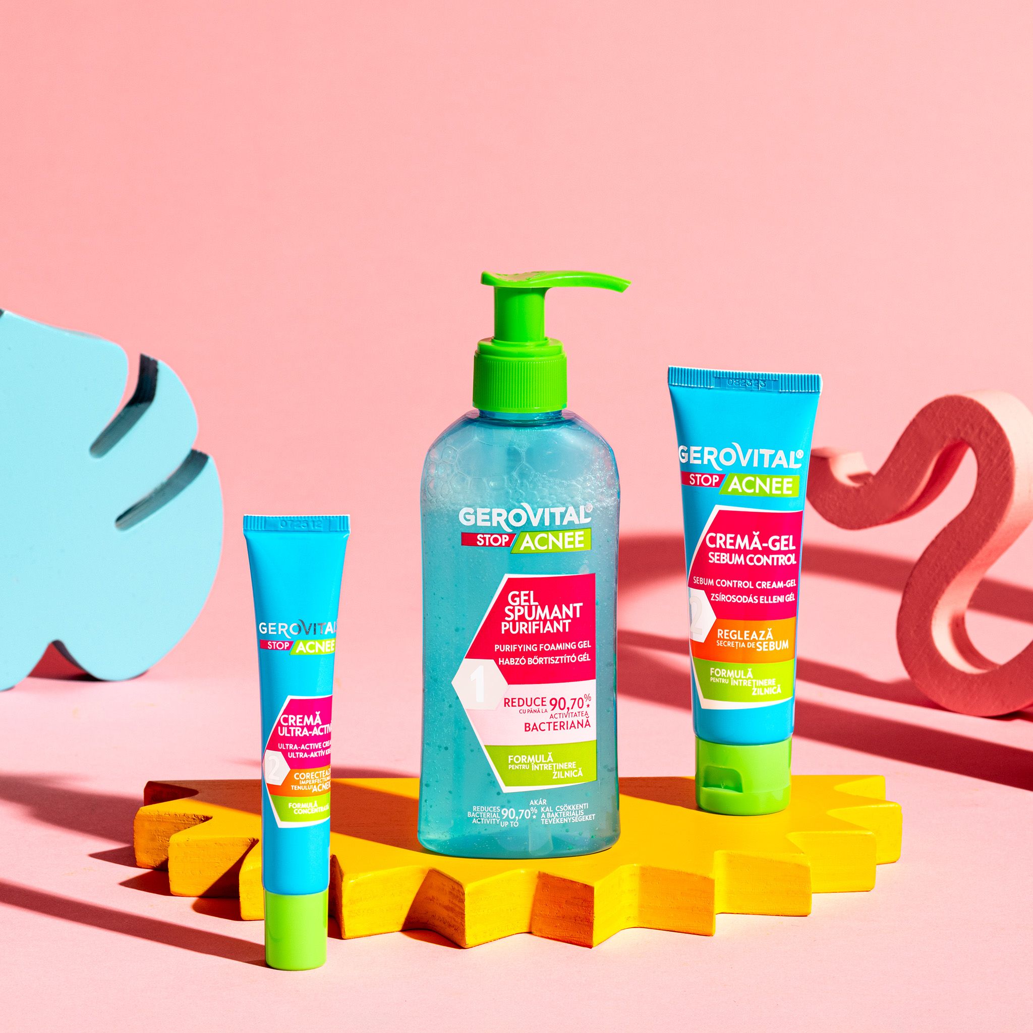 Tre prodotti: gel detergente, crema, crema-gel. Flaconi e tubi turchesi e verdi. Sfondo rosa con forme.