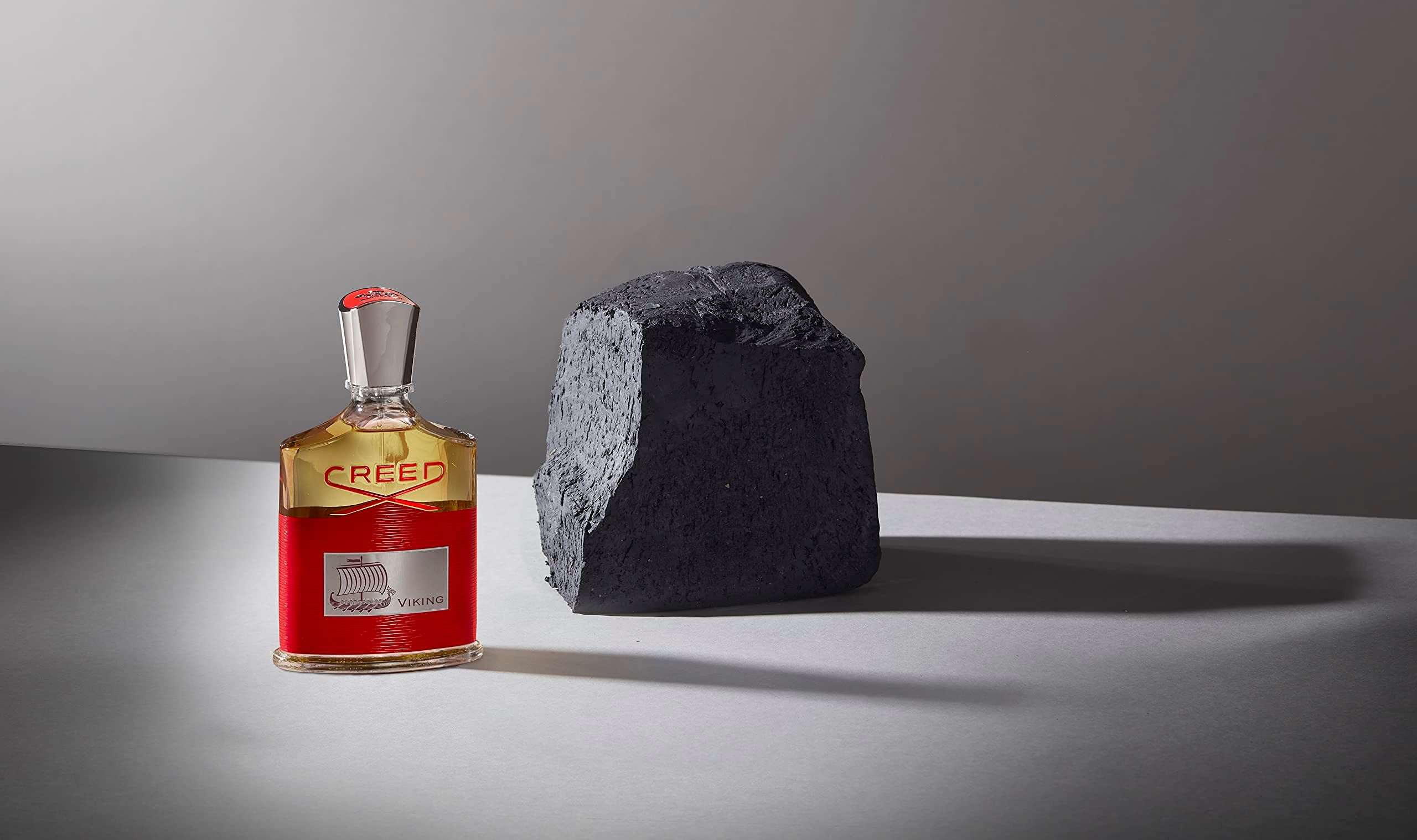 Flacone di profumo accanto a una pietra nera. Sull'etichetta è scritto "VIKING". Il flacone ha un tappo argentato.