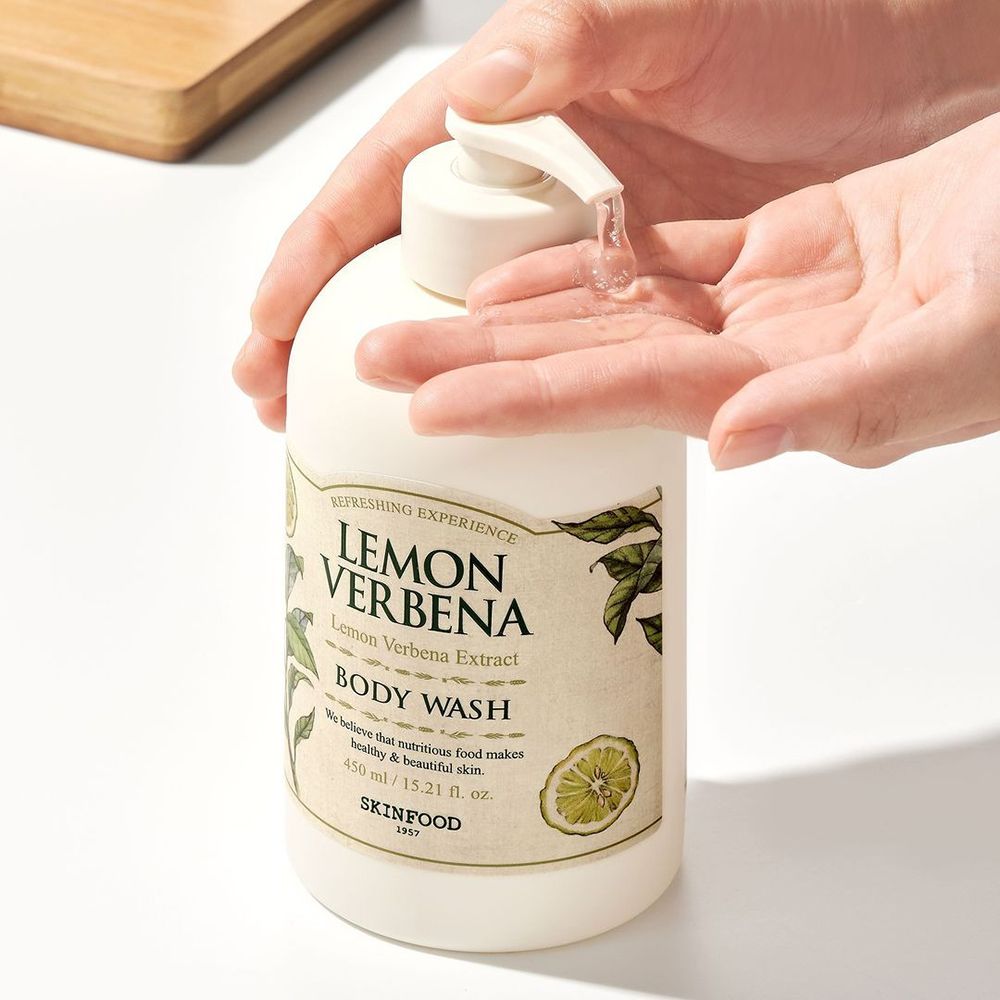 Flacone beige con dosatore. Scritta: Lemon Verbena Body Wash. Liquido trasparente erogato sulla mano.