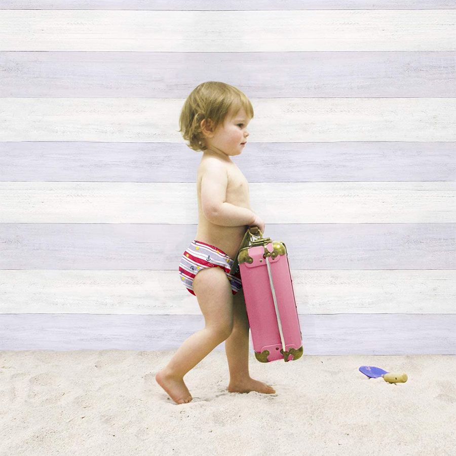 Bambino con costumino e valigia sulla spiaggia. Costumino a righe.