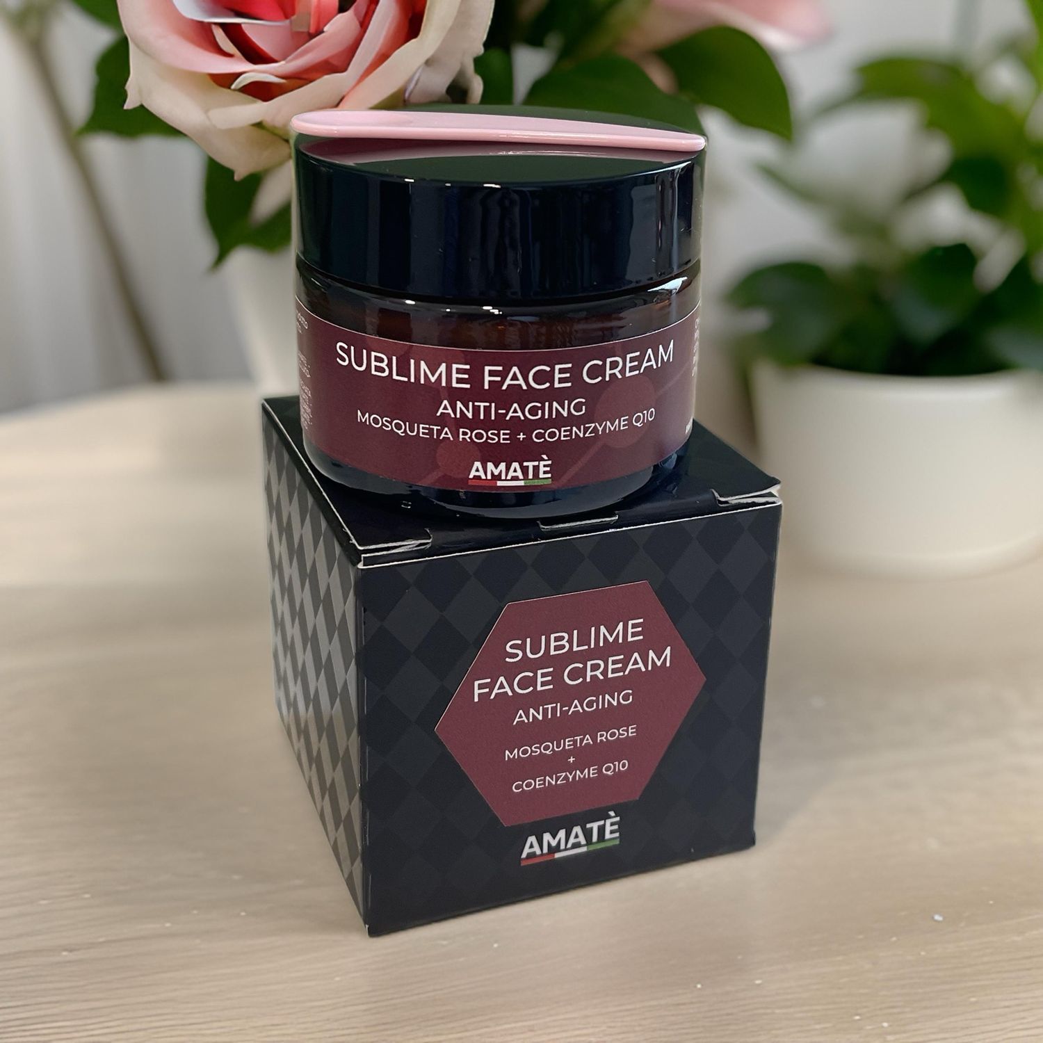 Vaso di crema e confezione. Scritta: Sublime Face Cream Anti-Aging, Mosqueta Rose + Coenzyme Q10, AMATÈ. Confezione nera con motivo. Fiori.