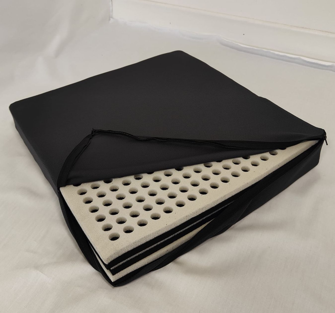 Fodera nera per sedile con cerniera, parzialmente aperta, che mostra un sedile multistrato in schiuma chiara forata.