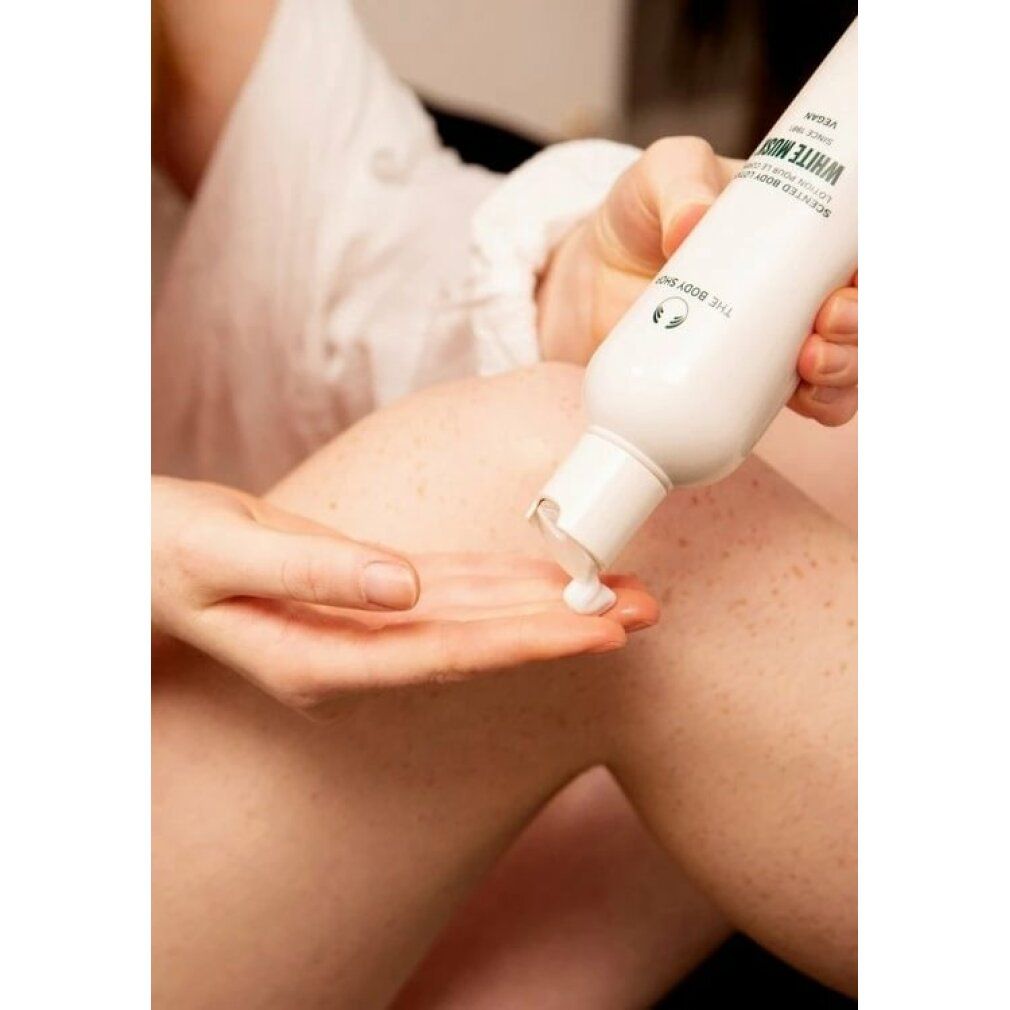 Persona versa crema da flacone bianco con testo White Musk sulla mano. Gamba sullo sfondo.