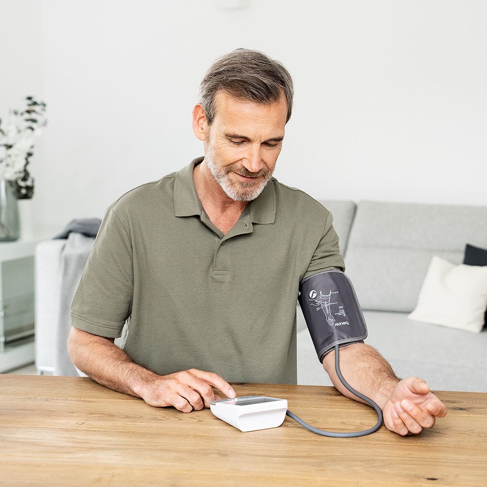 Uomo che utilizza un misuratore di pressione sul braccio. Il dispositivo è su un tavolo. Bracciale sul braccio. Bracciale grigio.