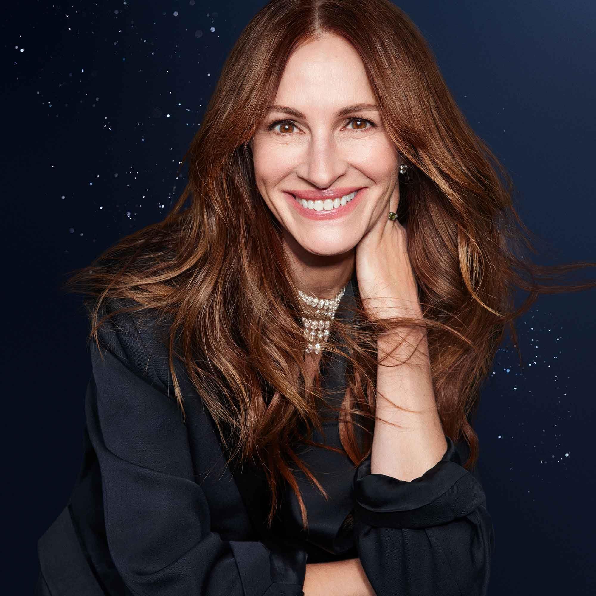 Ritratto di donna con lunghi capelli castani. Indossa una collana e sorride. Sfondo scuro con stelle.