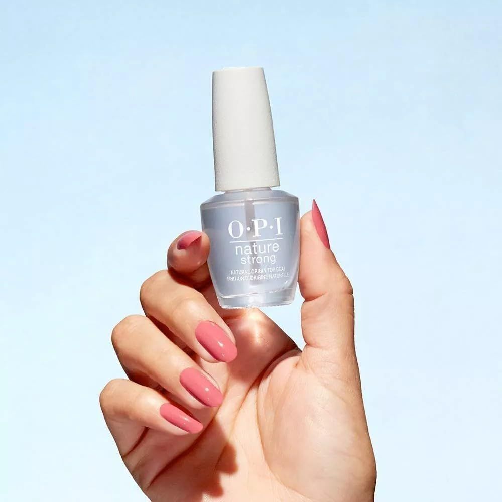 Mano che tiene un flacone di smalto. Logo O.P.I. Nature Strong visibile. Sfondo blu. Unghie con smalto rosa.