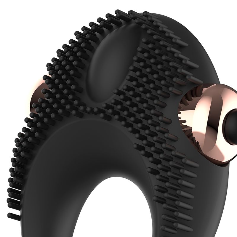 Primo piano dell'anello vibrante per pene in silicone nero. Borchie in rilievo e due elementi oro rosa.