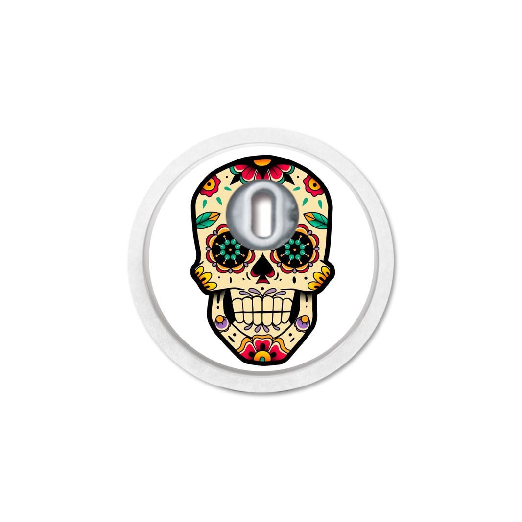 Adesivo rotondo con disegno di teschio. Apertura per sensore. Motivi floreali colorati. Bordo bianco.