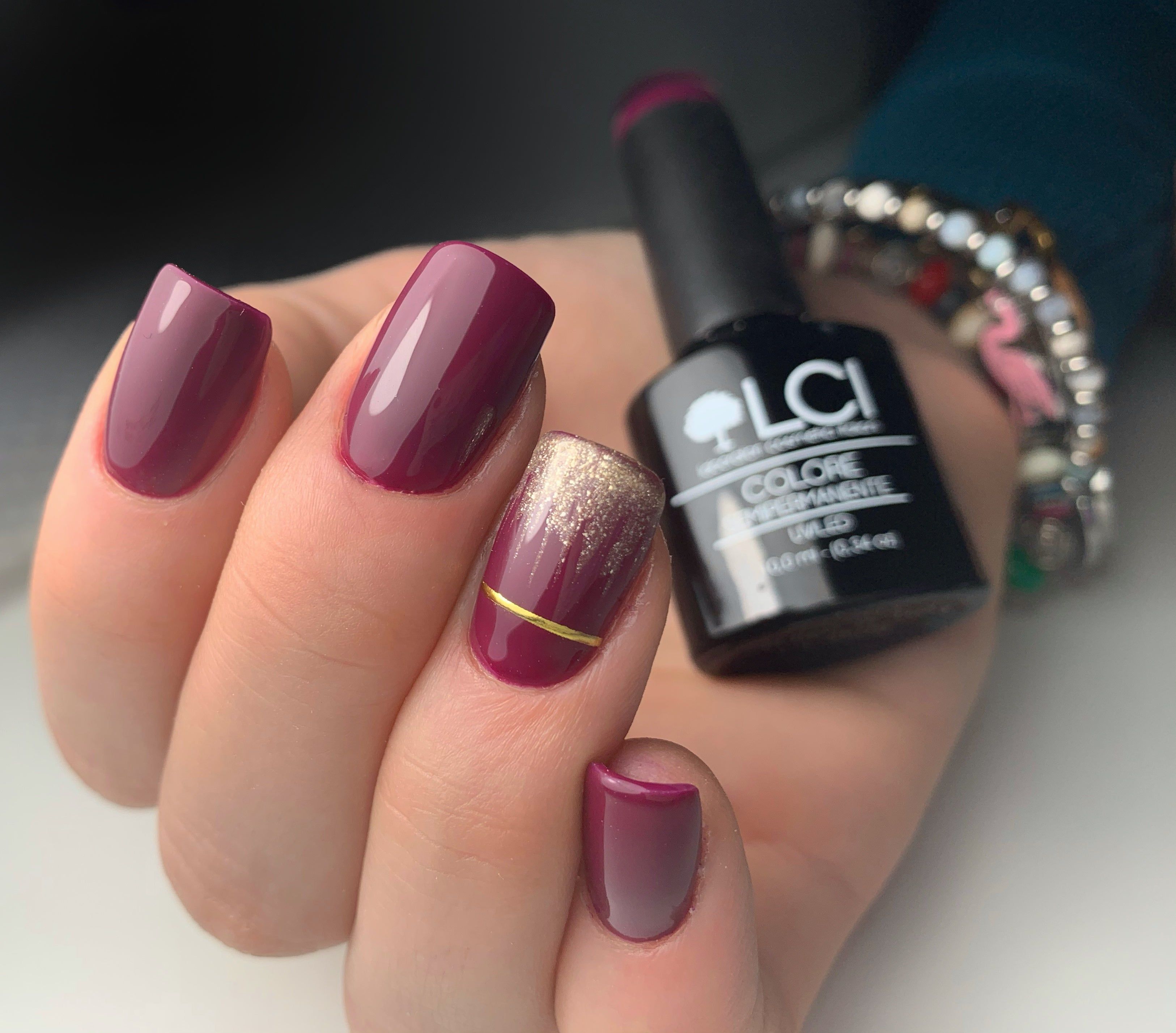Mano con unghie smaltate in diverse tonalità di rosso. Accanto, un flacone di smalto. Scritta: LCI, COLORE SEMIPERMANENTE.