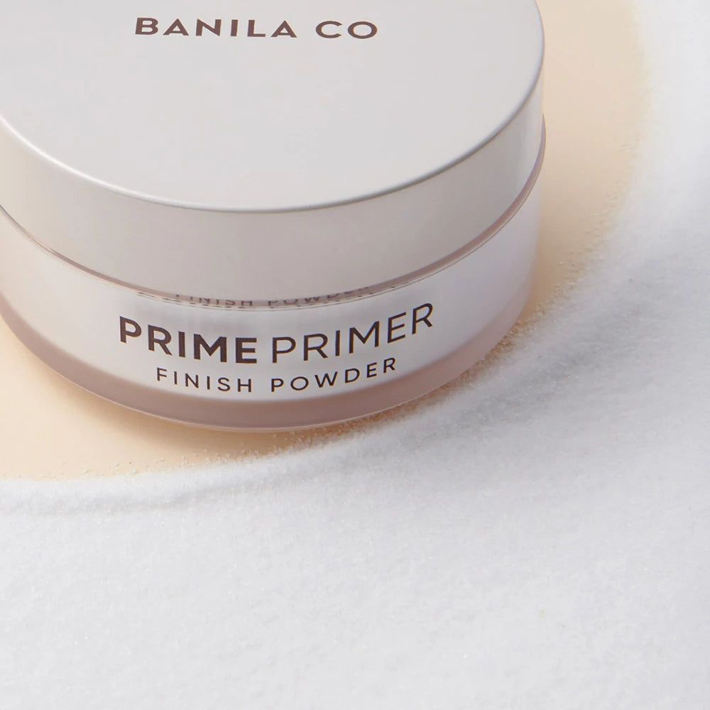 Vasetto bianco rotondo con coperchio. Scritta: BANILA CO, PRIME PRIMER FINISH POWDER. Primo piano.