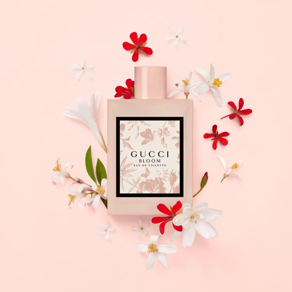 Flacone rosa con stampa floreale, circondato da fiori. Scritta: Gucci Bloom Eau de Toilette.