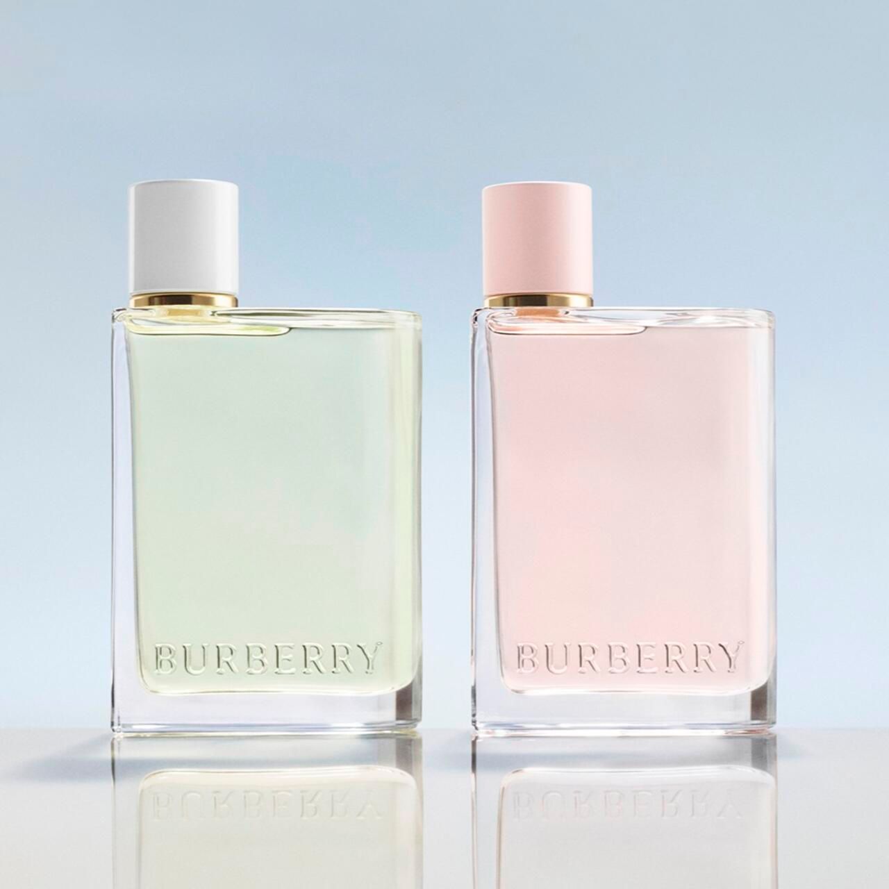 Due flaconi Burberry Her. Uno verde, uno rosa. Forma quadrata, tappo bianco, colletto dorato. Logo Burberry.