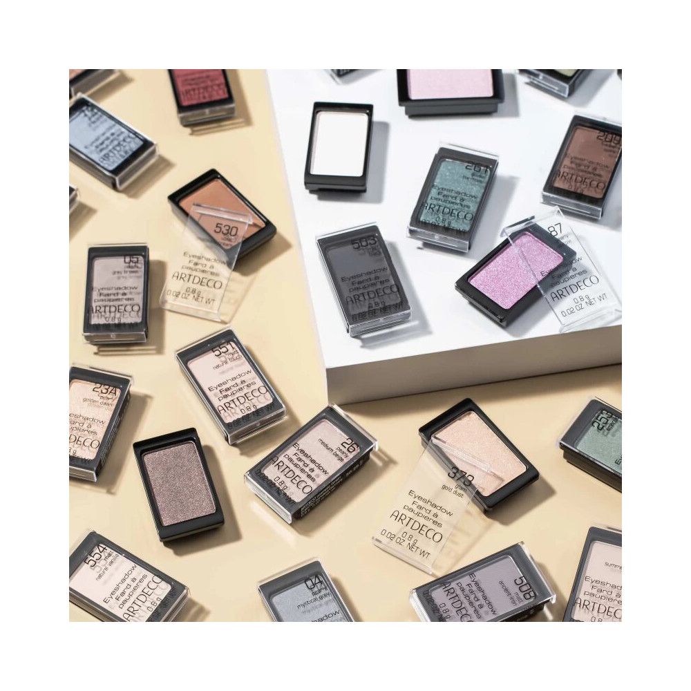 Artdeco Lidschatten Matt. Vari colori in contenitori neri con coperchi trasparenti. Su sfondo giallo.