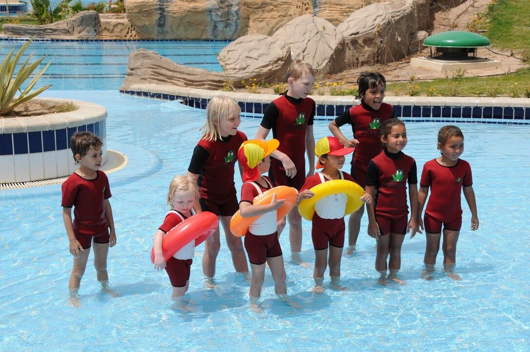 Bambini in piscina con Schwimmtrainer. Alcuni indossano Schwimmtrainer arancioni, altri gialli.