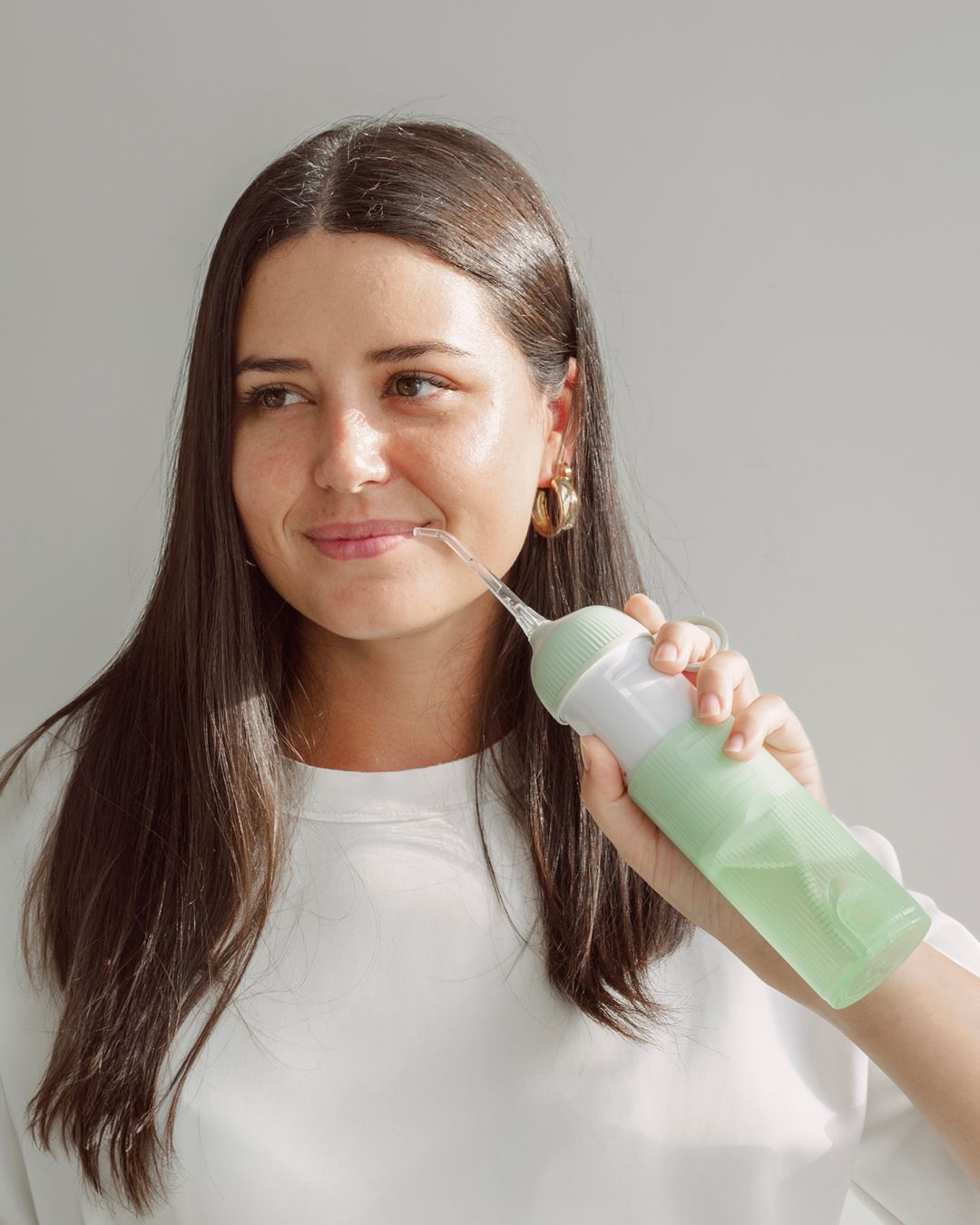 Donna con idropulsore. Idropulsore verde, parte centrale bianca. Orecchini dorati. Sfondo chiaro.