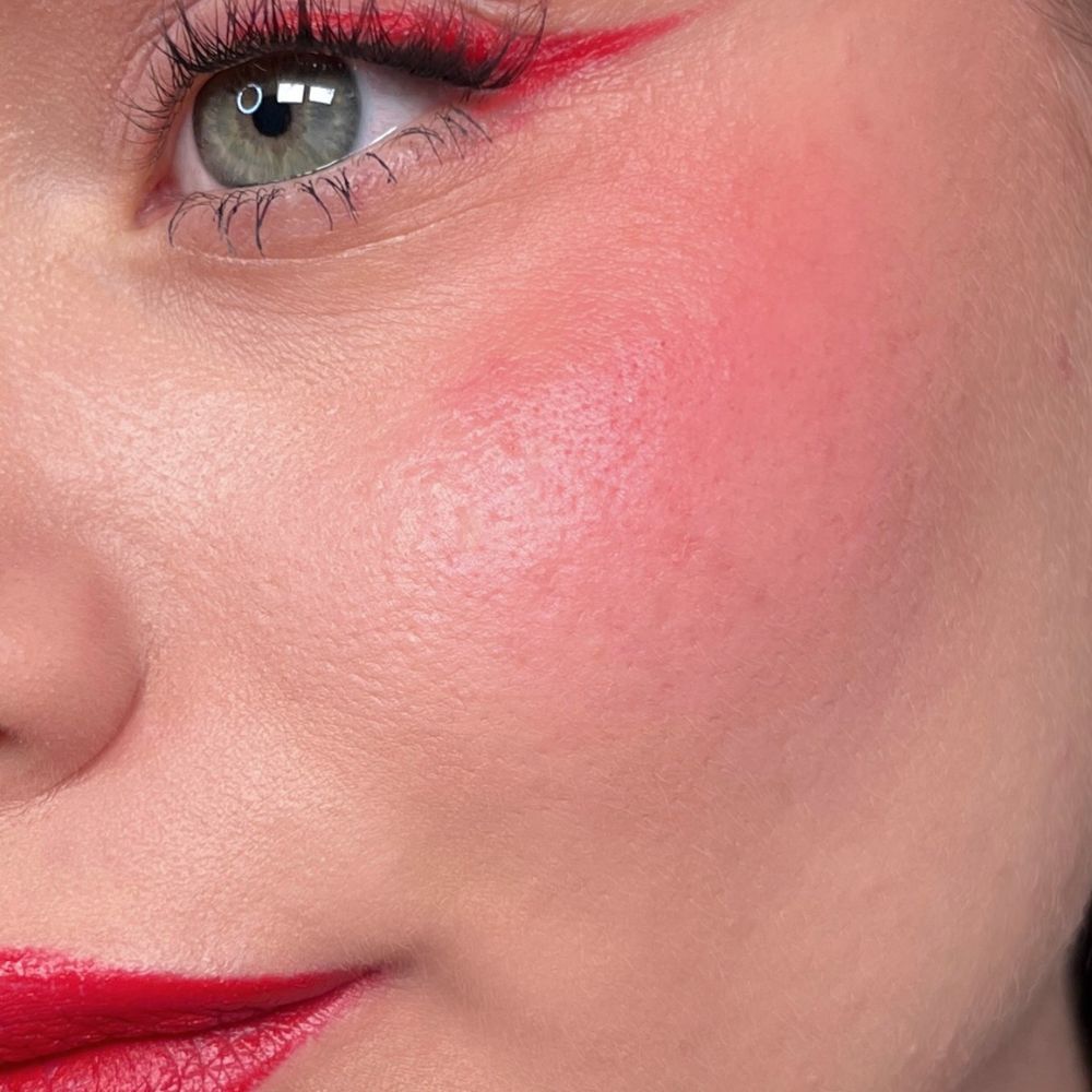 Primo piano di un viso con rossetto, eyeliner e fard rossi. Occhio verde. Prodotto: ALL TIGERS.