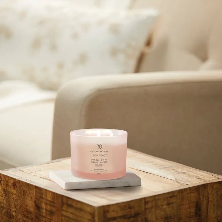 Candela rosa su tavolo. Scritta 'Chesapeake Bay'. Testo: 'stillness + purity', 'rose water'. 3 stoppini.