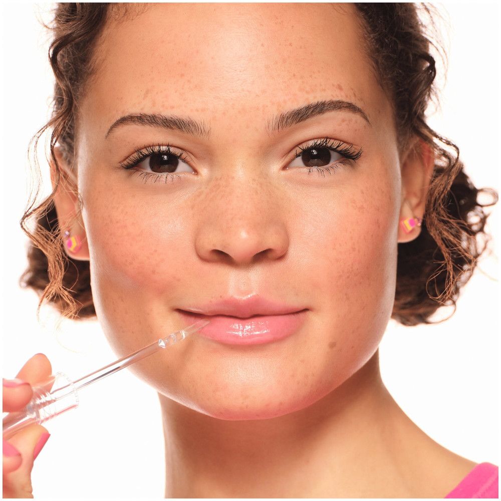 Primo piano di un viso. Lucidalabbra applicato sulle labbra. Pelle chiara, lentiggini, rossetto rosa.