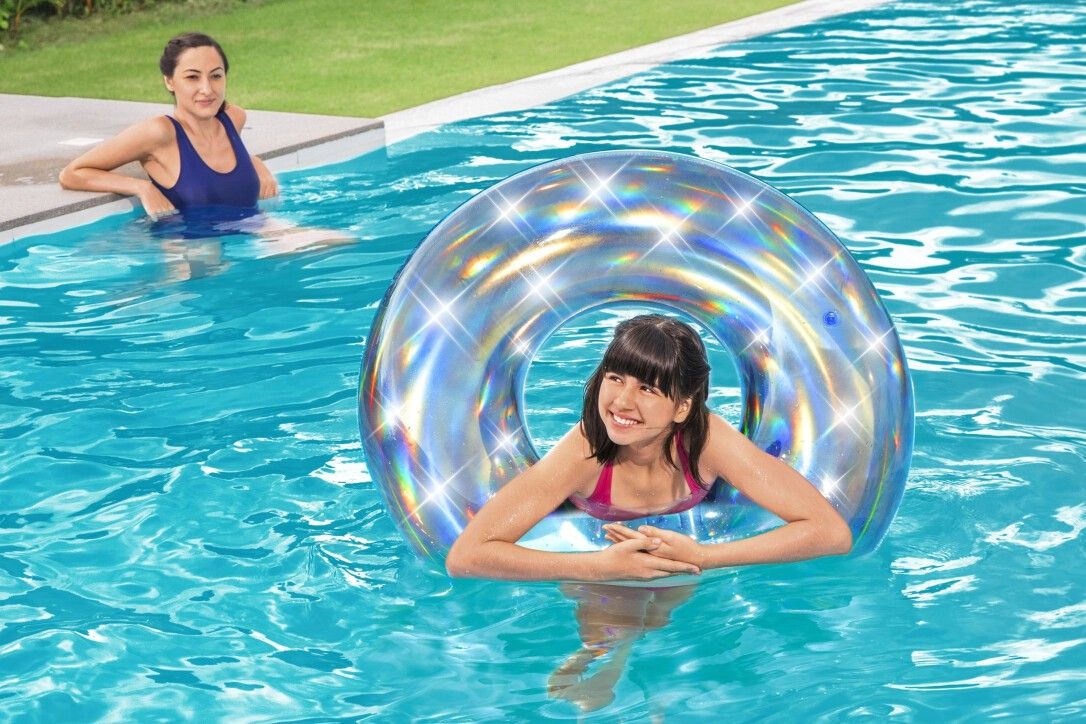 Ragazza e donna in piscina con anello da nuoto iridescente. Argento con riflessi arcobaleno. Acqua blu.