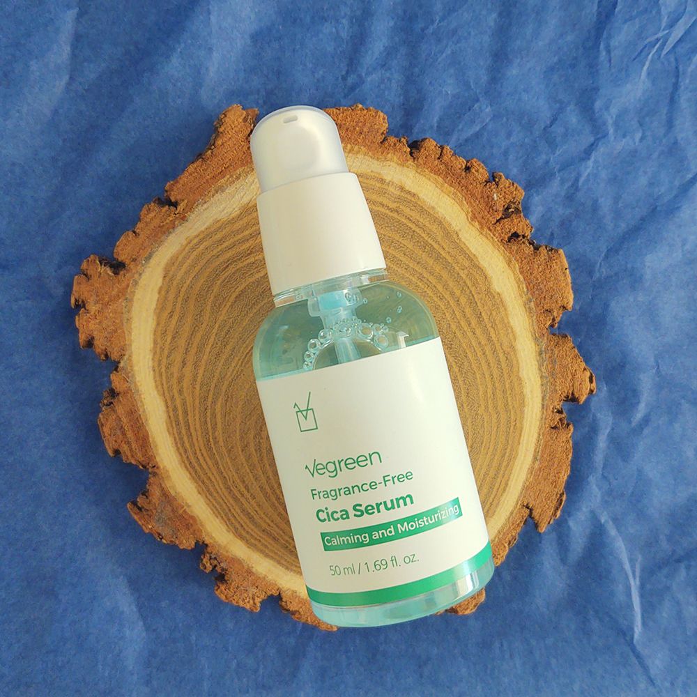 Flacone di siero per il viso su fetta di legno. Tappo a pompa bianco, etichette verdi e bianche. Liquido blu visibile.