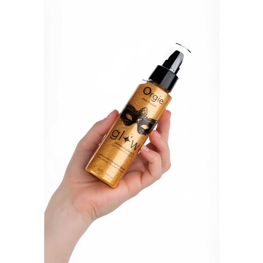 Flacone di olio per il corpo dorato, tenuto in mano. Scritta "Orgie" e "glow". Design maschera. Dosatore a pompa. Texture scintillante.