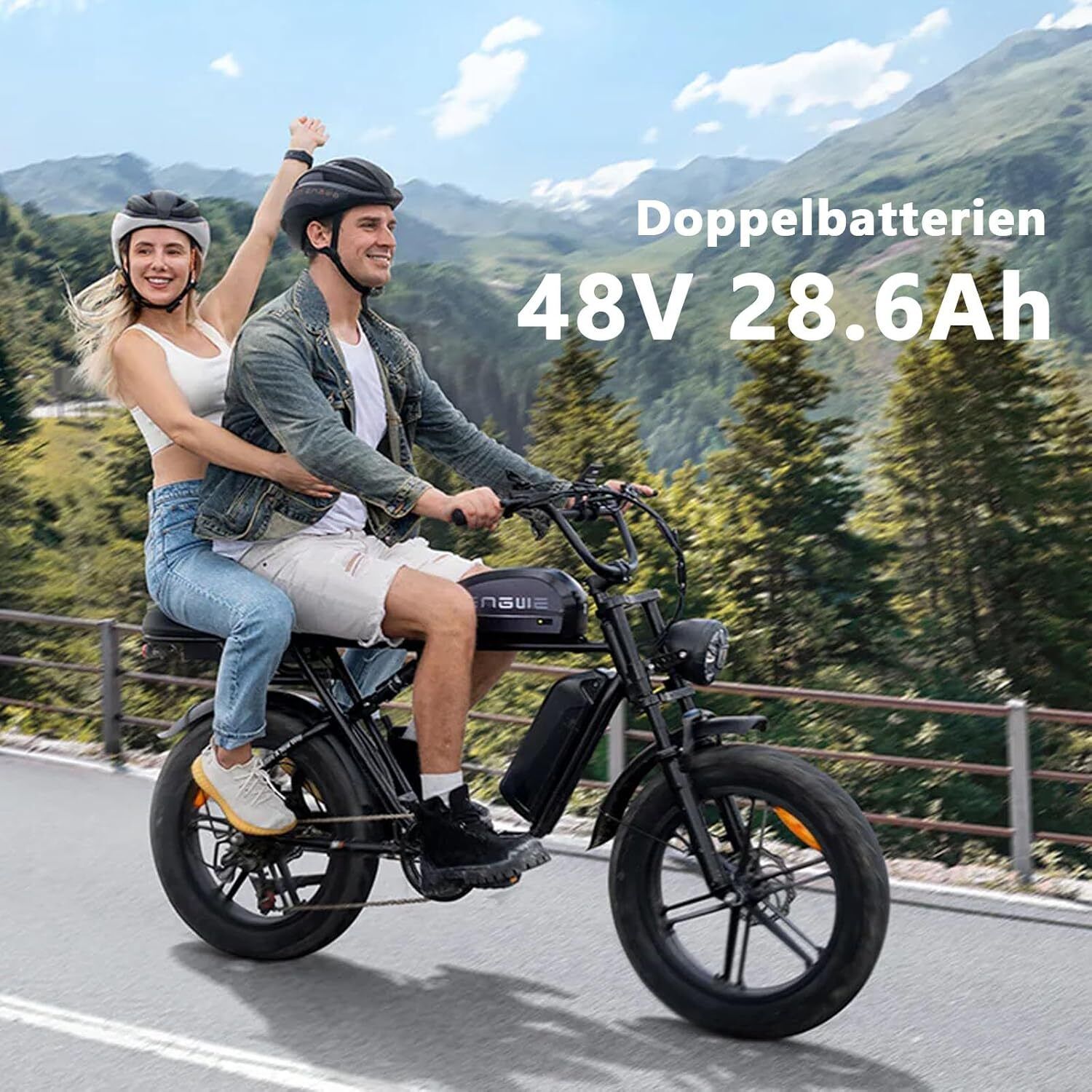 E-bike nero con due persone. Sul telaio "Doppelbatterien 48V 28.6Ah". Entrambi indossano caschi. Montagne sullo sfondo.