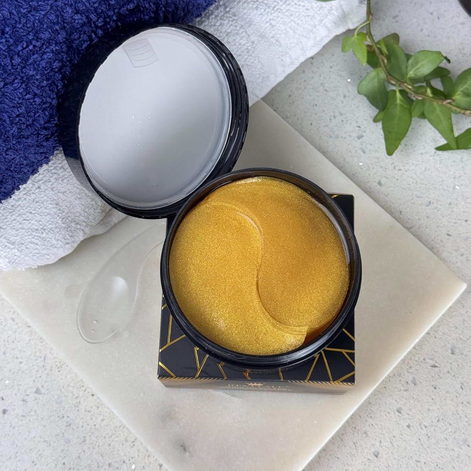 Barattolo nero aperto con patch dorati. Testo: Revitale Gold Under Eye Collagen Patches. 30 paia. Con spatola.