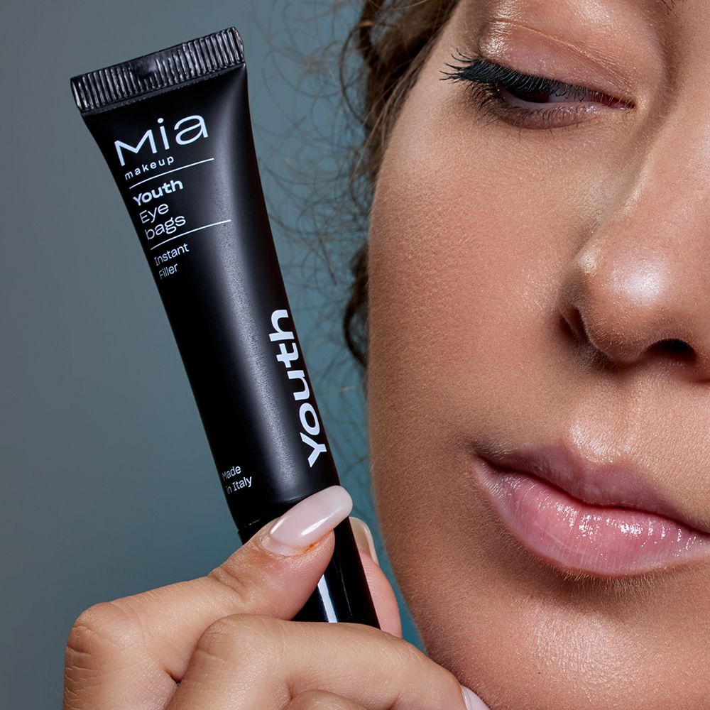 Donna tiene tubo nero. Marchio Mia Makeup. Nome: Youth Eye bags. Testo: Instant Filler. Made in Italy. Viso sullo sfondo.