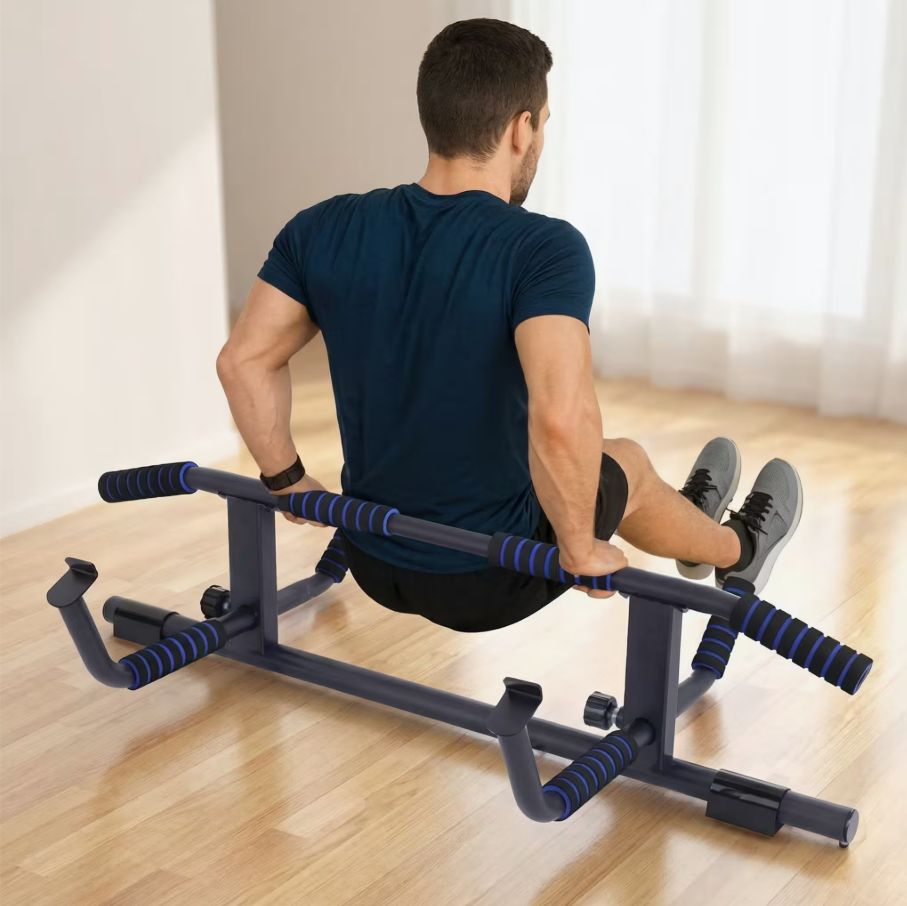 Uomo che si allena su una barra per trazioni. Struttura in metallo nero con maniglie blu. In piedi sul pavimento.